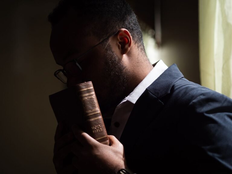 A man in a blue suit holds a Bible close, symbolizing contemplation and faith.
