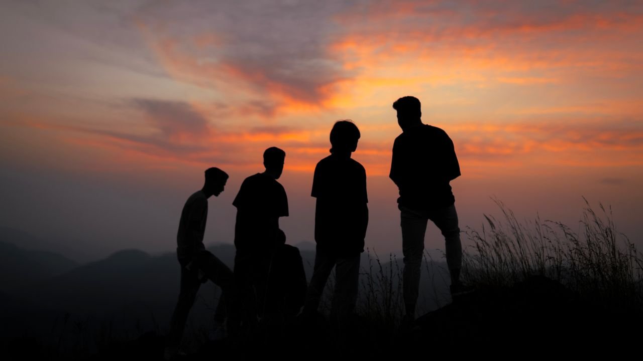 Silhouetted group of four people against a vibrant sunset sky.